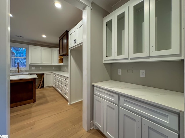 kitchen featuring light stone counters, light wood-type flooring, glass insert cabinets, and white cabinetry