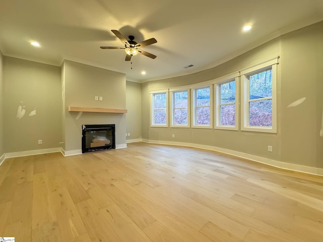 unfurnished living room featuring ornamental molding, light wood-type flooring, a glass covered fireplace, and visible vents