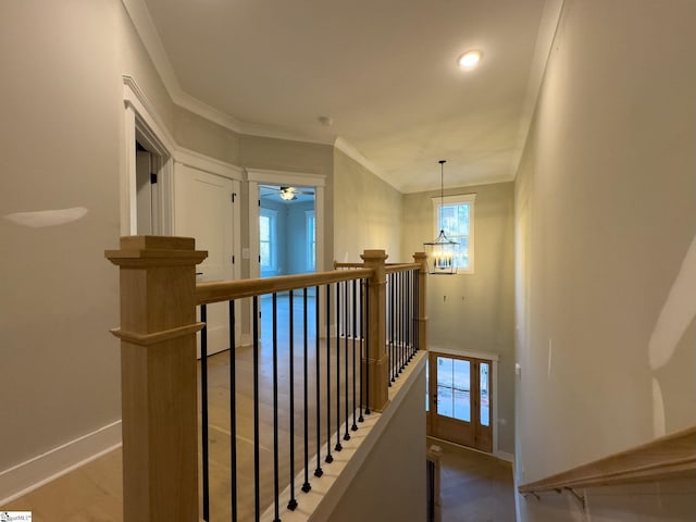 hallway with a notable chandelier, wood finished floors, an upstairs landing, baseboards, and ornamental molding