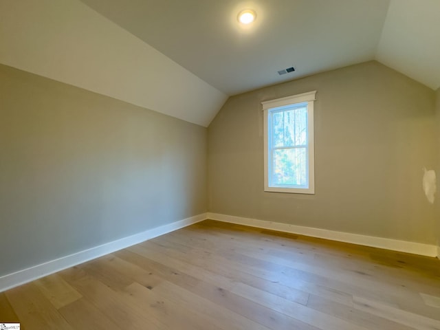 additional living space featuring light wood-type flooring, visible vents, vaulted ceiling, and baseboards