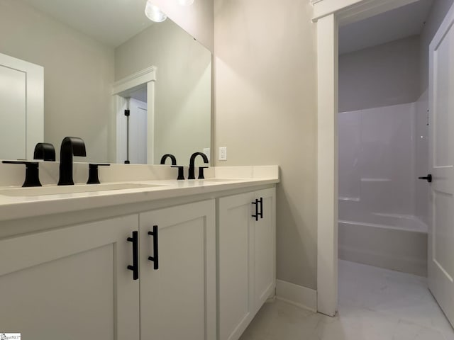 bathroom featuring marble finish floor, double vanity, a sink, and baseboards