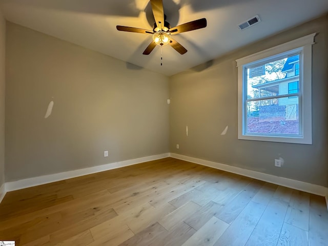 spare room featuring light wood finished floors, baseboards, visible vents, and a ceiling fan