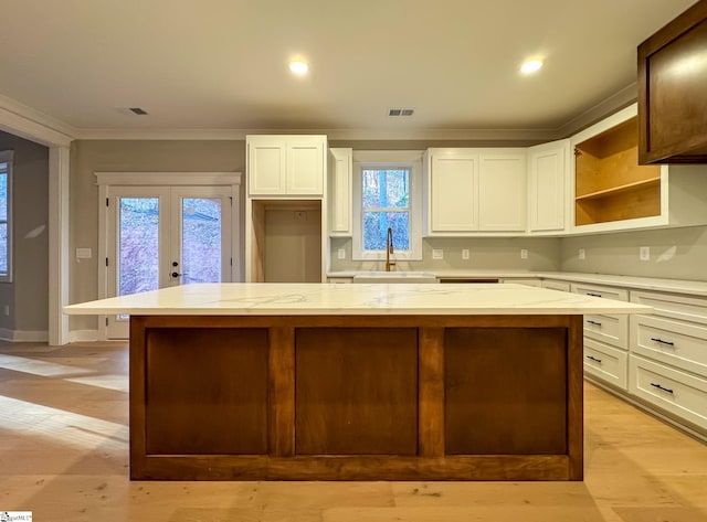 kitchen featuring visible vents, a kitchen island, white cabinetry, open shelves, and a sink