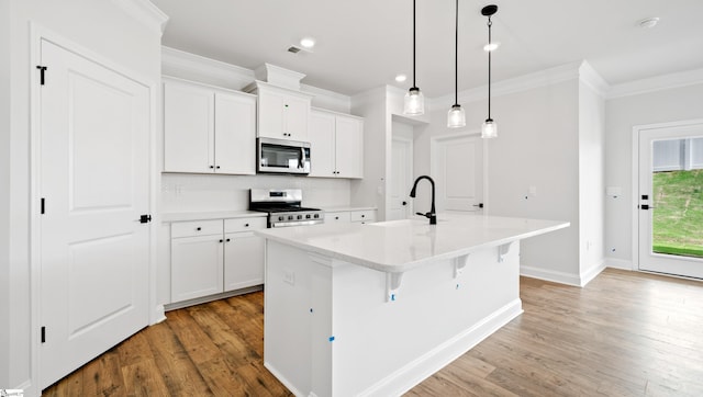 kitchen featuring appliances with stainless steel finishes, crown molding, a sink, light wood-style flooring, and a center island with sink