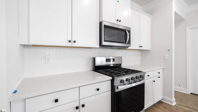 kitchen with appliances with stainless steel finishes, crown molding, decorative backsplash, wood finished floors, and white cabinetry
