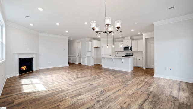 unfurnished living room featuring crown molding, a chandelier, light wood finished floors, recessed lighting, and baseboards