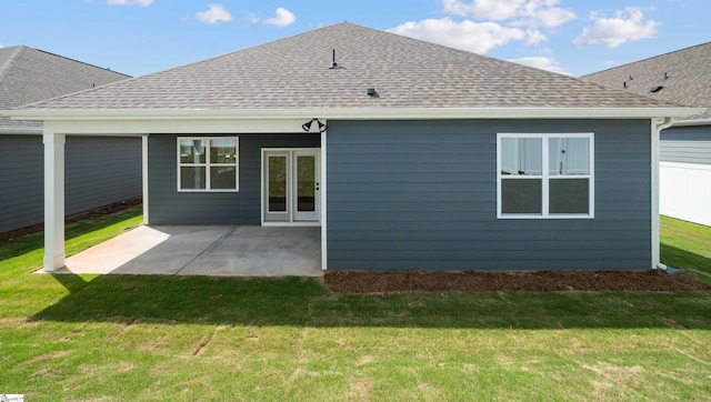 rear view of house with roof with shingles, a yard, and a patio