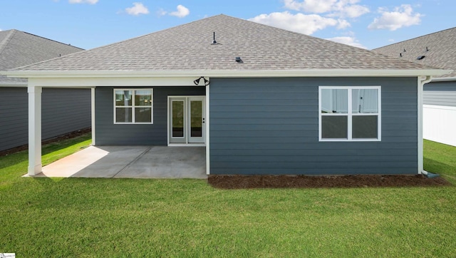 back of house with roof with shingles, a lawn, and a patio