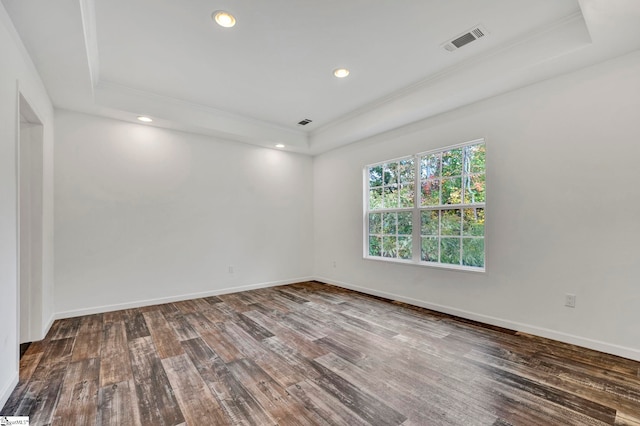 unfurnished room with a tray ceiling, wood finished floors, visible vents, and baseboards