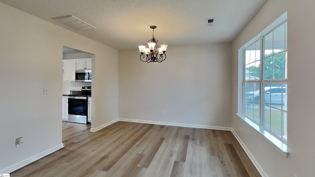 unfurnished dining area with light hardwood / wood-style floors, a wealth of natural light, and a notable chandelier