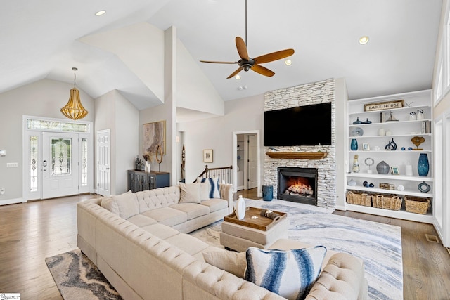 living room featuring high vaulted ceiling, built in shelves, a fireplace, light hardwood / wood-style floors, and ceiling fan