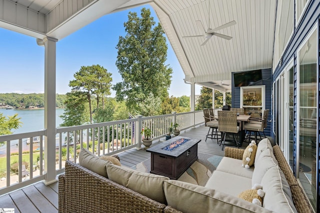 wooden deck featuring ceiling fan, an outdoor living space with a fire pit, and a water view