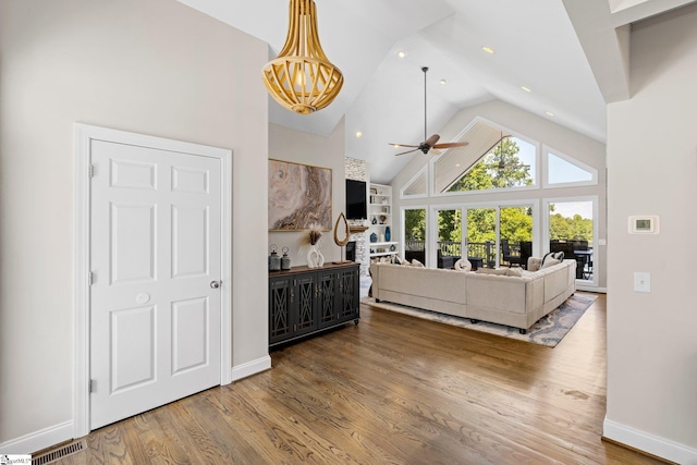 living room with ceiling fan with notable chandelier, hardwood / wood-style flooring, and high vaulted ceiling