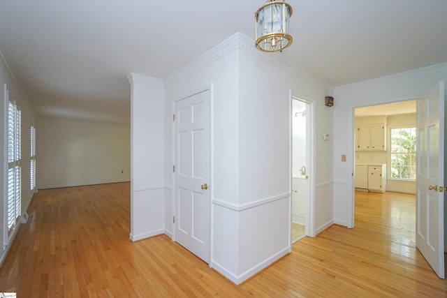 corridor with a notable chandelier, crown molding, and light hardwood / wood-style flooring