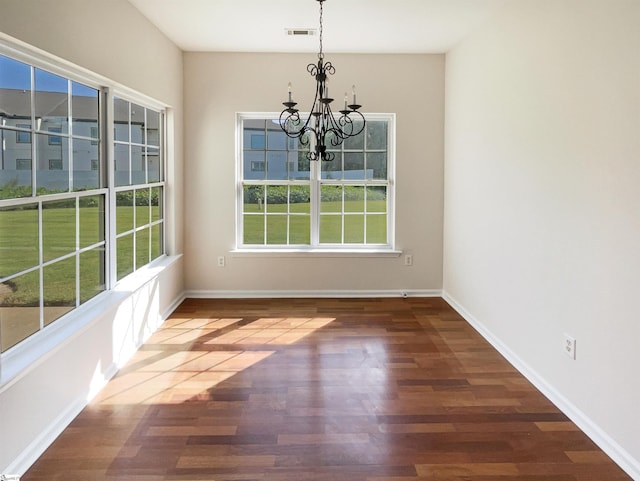 unfurnished dining area featuring a notable chandelier, baseboards, visible vents, and wood finished floors