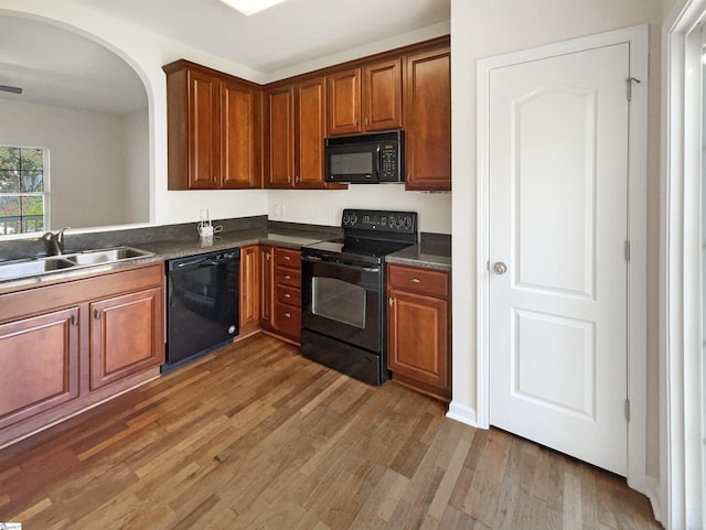 kitchen with dark countertops, brown cabinets, wood finished floors, black appliances, and a sink