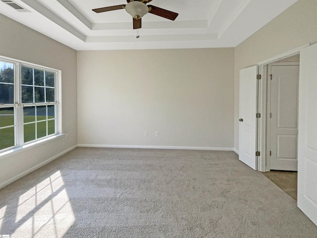 carpeted spare room featuring a ceiling fan, a raised ceiling, visible vents, and baseboards