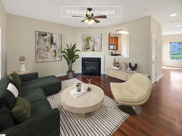 living area featuring baseboards, a fireplace with flush hearth, visible vents, and dark wood-type flooring