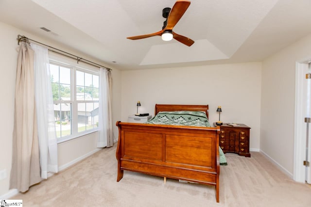 bedroom with ceiling fan, light carpet, and a tray ceiling