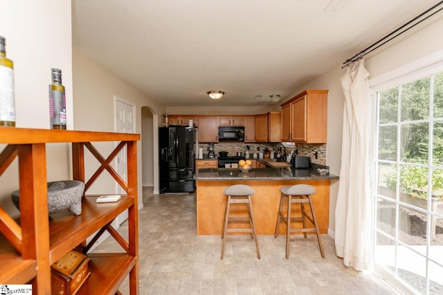 kitchen featuring tasteful backsplash, a breakfast bar area, kitchen peninsula, black appliances, and light tile patterned flooring