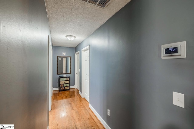 corridor featuring light wood-type flooring and a textured ceiling