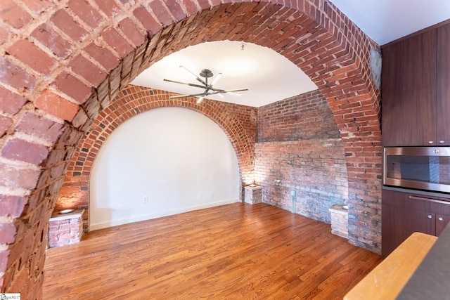 unfurnished living room with light wood-style floors, ceiling fan, and brick wall