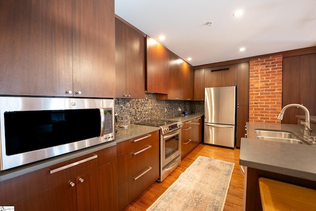 kitchen with brick wall, stainless steel appliances, sink, and light hardwood / wood-style flooring