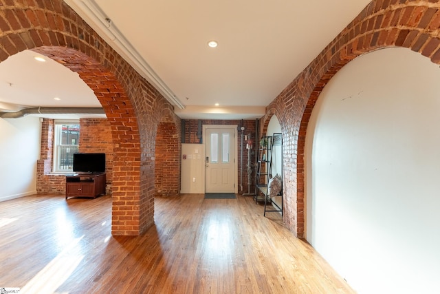 unfurnished living room with light wood-type flooring, brick wall, arched walkways, and recessed lighting