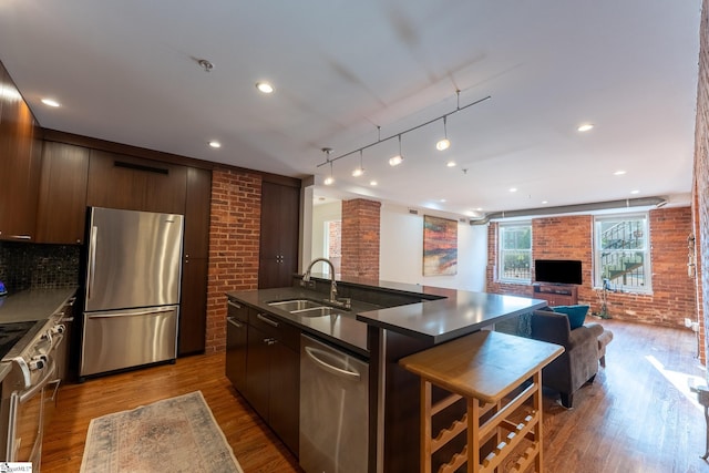 kitchen featuring dark brown cabinets, wood-type flooring, sink, appliances with stainless steel finishes, and a center island with sink