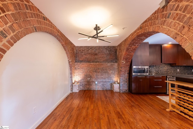 unfurnished living room featuring baseboards, brick wall, arched walkways, and wood finished floors