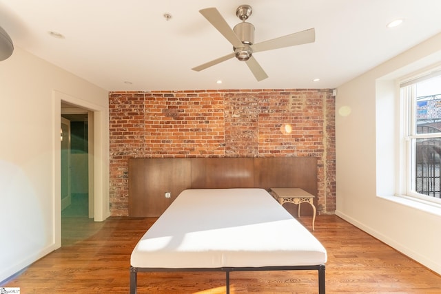 bedroom with light wood-type flooring, ceiling fan, a fireplace, and brick wall