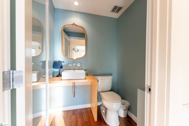 half bathroom with toilet, wood finished floors, vanity, visible vents, and baseboards