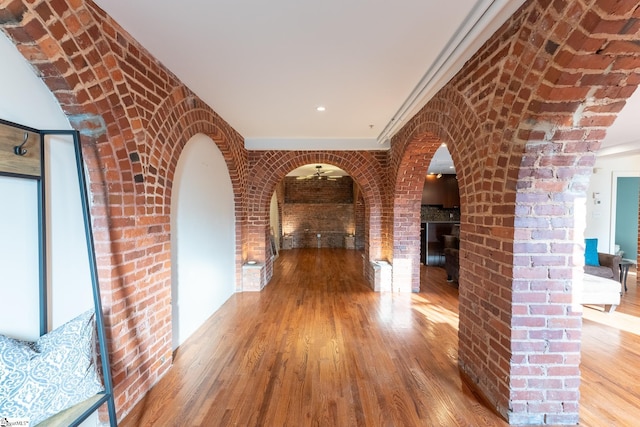 hallway featuring brick wall, arched walkways, and wood finished floors