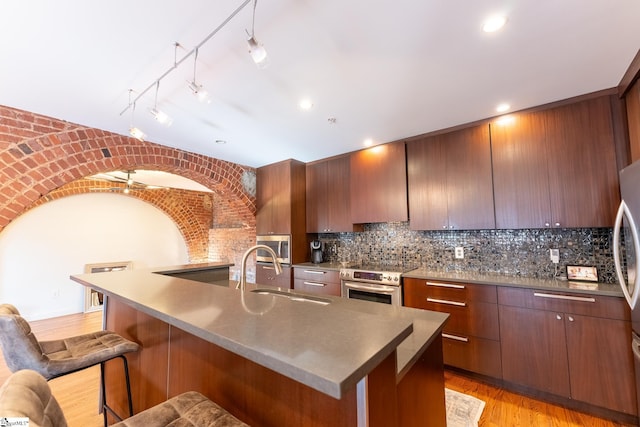 kitchen with track lighting, sink, decorative backsplash, appliances with stainless steel finishes, and light hardwood / wood-style floors