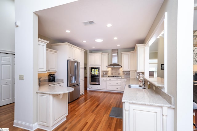 kitchen with visible vents, appliances with stainless steel finishes, a sink, a peninsula, and wall chimney exhaust hood