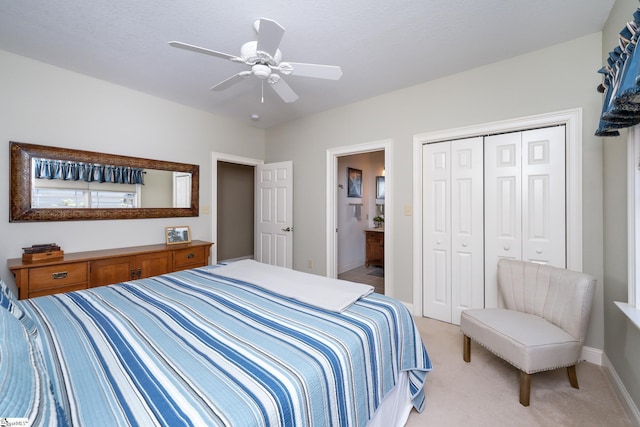 bedroom with light colored carpet, a ceiling fan, baseboards, a closet, and ensuite bath