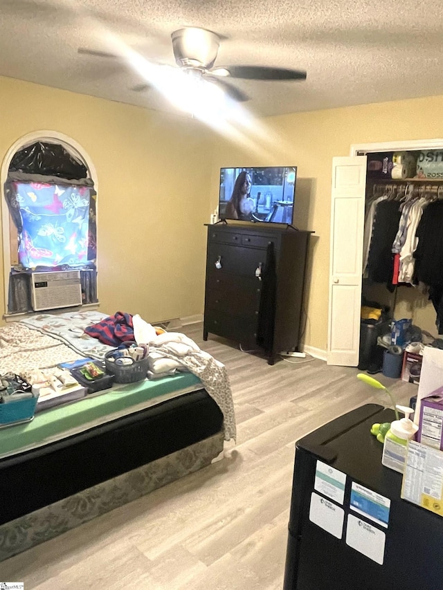 bedroom with a textured ceiling, cooling unit, ceiling fan, a closet, and light hardwood / wood-style floors