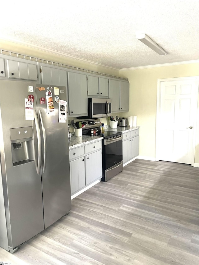 kitchen featuring light wood-type flooring, appliances with stainless steel finishes, light stone countertops, and a textured ceiling