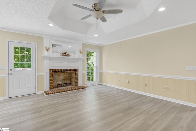 unfurnished living room with light wood-type flooring, a tray ceiling, wainscoting, and a healthy amount of sunlight