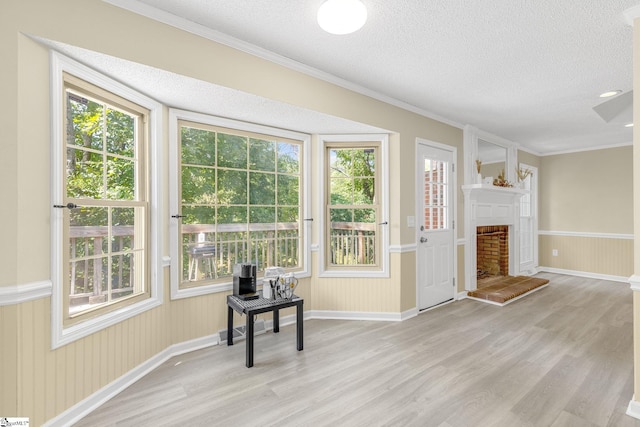 interior space with a textured ceiling, a fireplace with raised hearth, light wood-style flooring, wainscoting, and crown molding