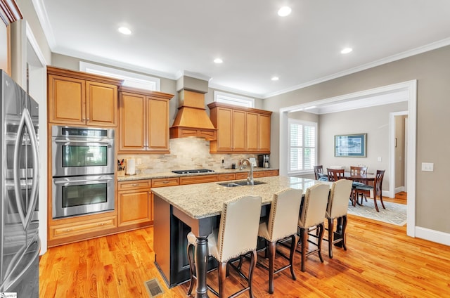 kitchen featuring light stone countertops, appliances with stainless steel finishes, tasteful backsplash, an island with sink, and light wood-type flooring