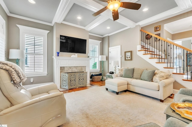 living room with a tiled fireplace, crown molding, light hardwood / wood-style flooring, coffered ceiling, and ceiling fan