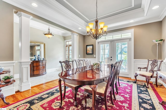 dining room featuring crown molding, light hardwood / wood-style flooring, ornate columns, and a tray ceiling