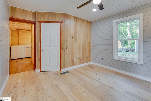 empty room with washing machine and clothes dryer, ceiling fan, wood walls, and light wood-type flooring