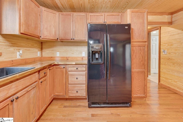 kitchen featuring light hardwood / wood-style floors, light brown cabinets, black fridge, wooden counters, and wooden walls