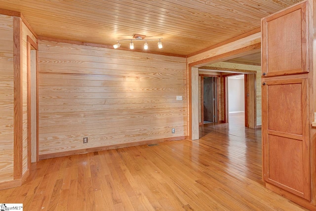 empty room featuring wooden walls, light wood-type flooring, wooden ceiling, and track lighting