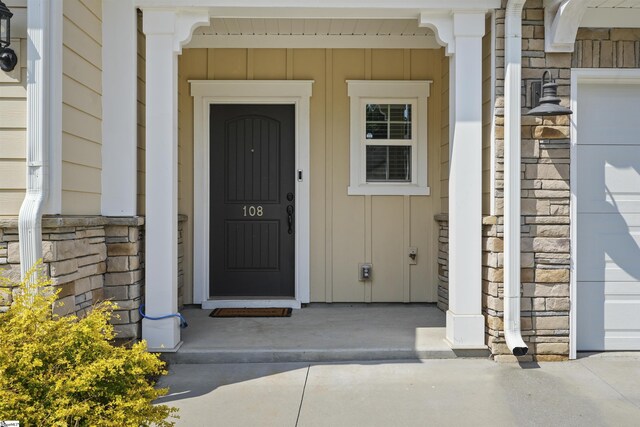 entrance to property featuring a garage, stone siding, and board and batten siding