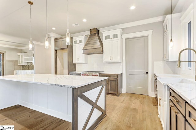 kitchen with pendant lighting, premium range hood, backsplash, light hardwood / wood-style floors, and white cabinets