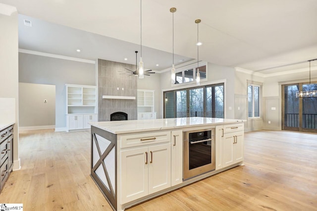 kitchen with a tiled fireplace, ceiling fan with notable chandelier, oven, light stone countertops, and light hardwood / wood-style floors