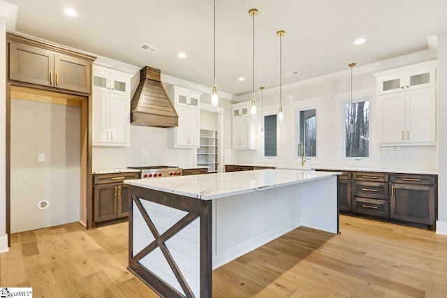 kitchen featuring hanging light fixtures, a center island, light wood-type flooring, custom exhaust hood, and white cabinetry